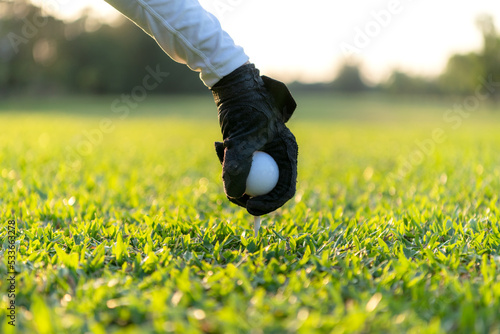 Close up hand asian sporty woman putting golf ball on tee with club in golf course on evening on time for healthy sport. Lifestyle and Sport Concept.