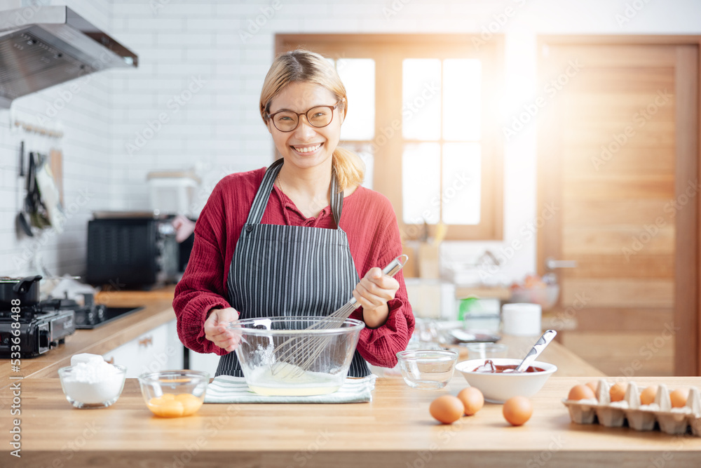 Beautiful young woman is mixing batter, looking at camera and smiling while baking in kitchen at home ,decorating a cake of chocolate cake,cooking class, culinary, bakery, food and people concept Beautiful young woman is mixing batter, looking at camera and smiling while baking in kitchen at home ,decorating a cake of chocolate cake,cooking class, culinary, bakery, food and people concept