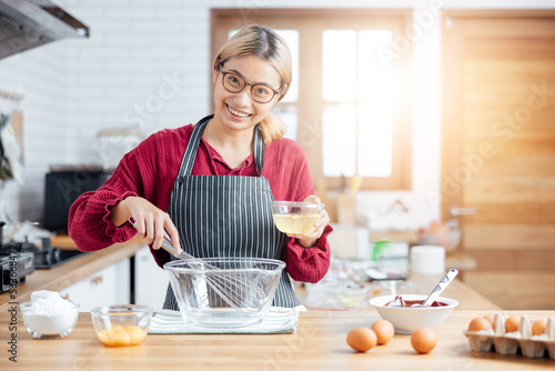 Beautiful young woman  is mixing batter, looking at camera and smiling w hile baking in kitchen at home ,decorating a cake of chocolate cake,cooking class, culinary, bakery, food and people concept photo
