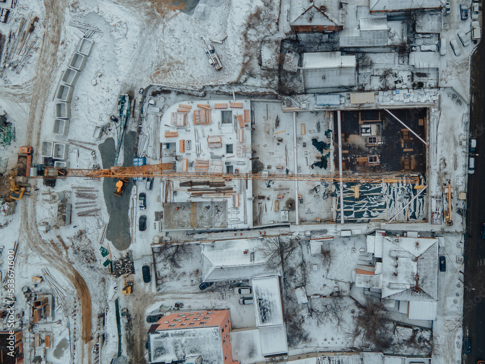 Construction of a new residential complex in winter. New housing. View of the construction site from above. Construction of a multi-storey building using a crane and concrete