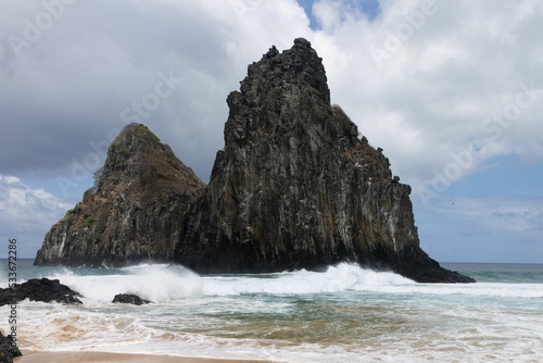 Foamy sea waves hitting sandy Cacimba do Padra beach with huge rock formations in the background photo