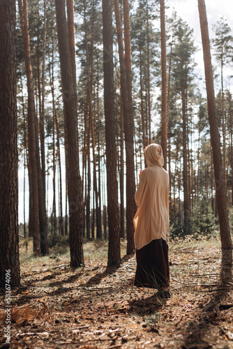 Caucasian Yogi girl in a hood and a long skirt in the autumn sunset forest relaxes, catches zen © Julia