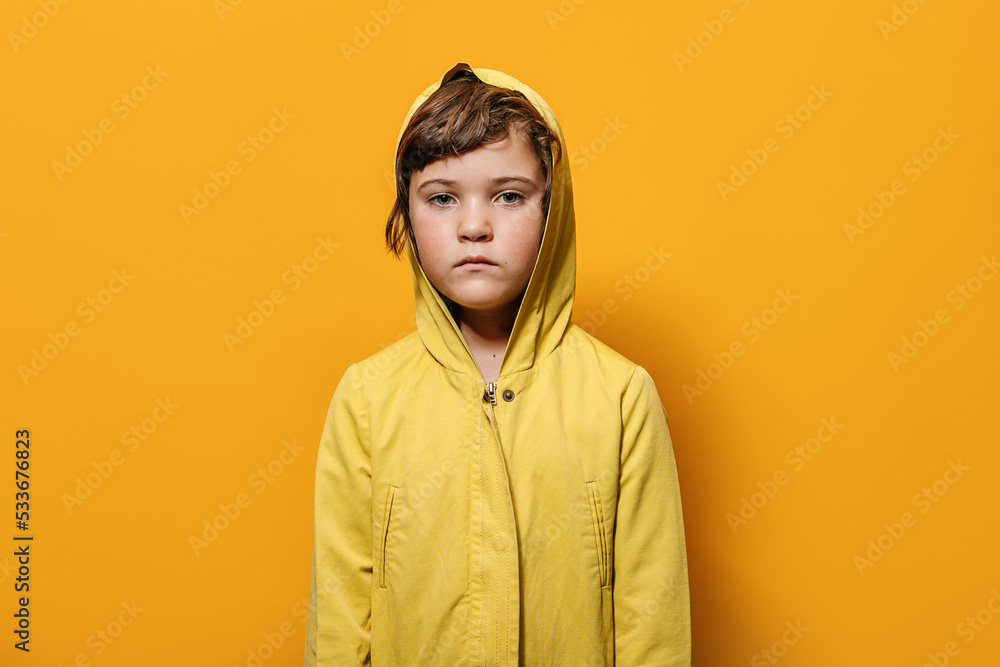 Upset little girl looking at camera against yellow wall in studio Upset little girl looking at camera against yellow wall in studio