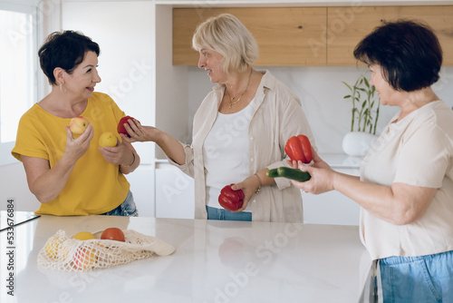 Happy senior women in kitchen cooking together. Mature women in kitchen have fun and prepare salad. photo