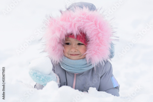 Kid playing with snowballs in fortress. Little cute ruddy girl with red cheeks throwing snow, building snowman. Family Christmas vacation with child in frosty winter Park. Wintertime, active outdoor