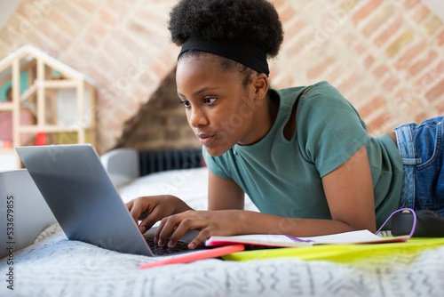 Teenager doing homework on a laptop in her room
