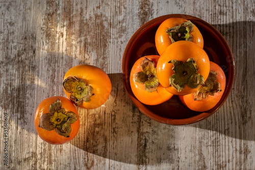 Aerial view of ripe persimmon fruits in a clay container on a rustic wooden table.