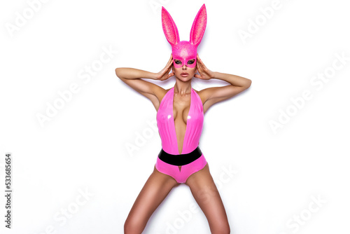 Sexy blonde woman posing in Halloween latex pink costume and pink bunny mask on white background. Halloween costume.