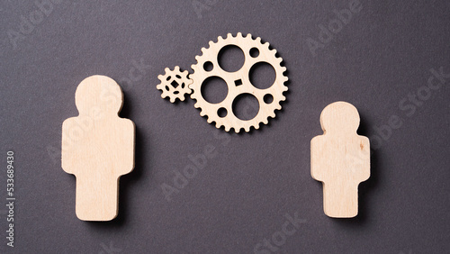 Two gears rotate between two wooden silhouettes of people Concept of teamwork photo
