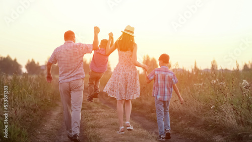 Parents playing with boy siblings walk among wheat fields and explore countryside aesthetic. Family enjoys spending summer holidays together at sunset, sunlight