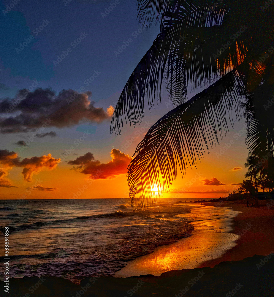 Sun slowly setting into the Caribbean Sea, Maxwell Beach, Barbados.  - obrazy, fototapety, plakaty 