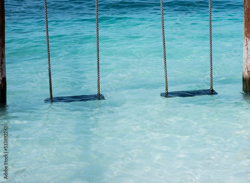 Two empty swings on the water by the sea at a tropical beach. Vacation travel concept