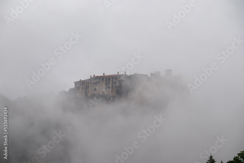 Panoramic view of Holy Monastery of Varlaam surrounded by misty fog on cloudy day, Kalambaka, Meteora, Thessaly, Greece, Europe. Dramatic landscape appearing. Landmark build on unique rock formations