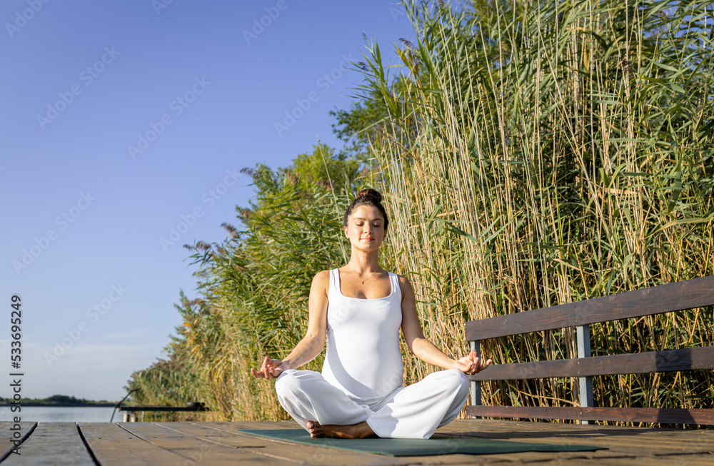 Pregnant woman doing yoga at lake during the day.