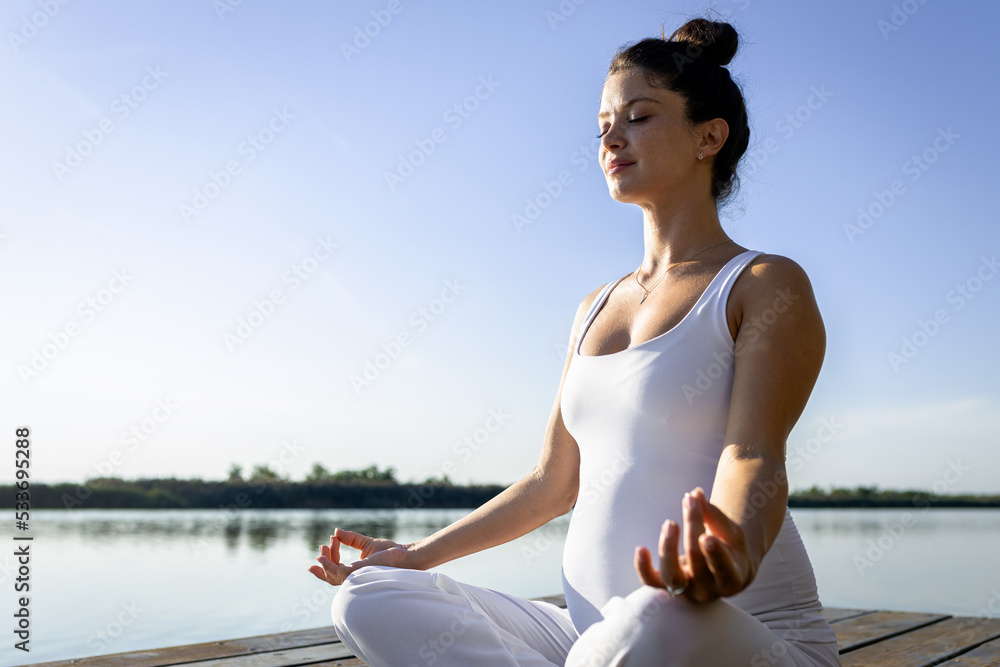 Pregnant woman doing yoga at lake during the day.