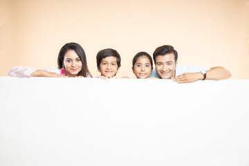 Advertising. happy indian family with white empty banner or poster billboard for content, place for text or image isolated on plane studio background