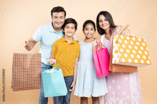 Portrait of happy indian family wearing casual cloths holding shopping bags and celebration diwali festival together isolated on studio background. Parents with kids celebrate festive season sale