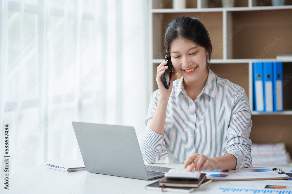 Charming and smiling Asian business woman Talk to customers on mobile phones and use their laptops to do office work. Charming and smiling Asian business woman Talk to customers on mobile phones and use their laptops to do office work.