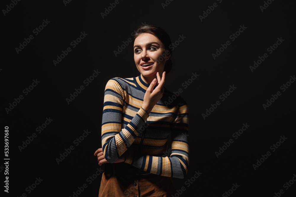 cheerful young woman in striped turtleneck and skirt looking away isolated on black. cheerful young woman in striped turtleneck and skirt looking away isolated on black.