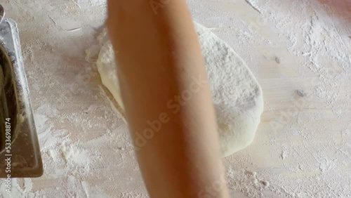 Woman's hands making a khachapuri base using rolling pin on the flour covered home table. Home Khachapuri - popular Georgian Caucasian cousine baked meal dough prepraration moment. 4K footage. photo