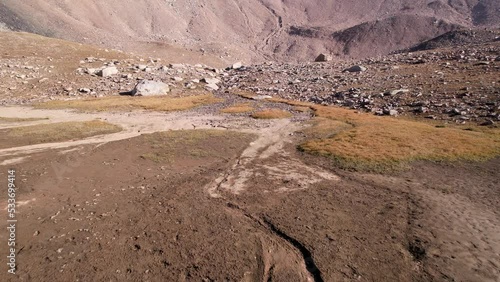 Drone view of a dried-up riverbed in the mountains. Shoe marks on wet sand. Yellow grass and big rocks. A steep gorge with an ascent to a mountain pass. Kazakhstan. Mountains of the Trans - Ili Alatau photo