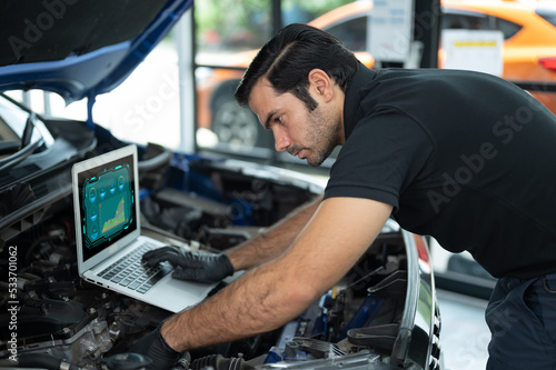 Mechanic Asian man close up using laptop computer and diagnostic software to tuning fixing repairing car engine automobile vehicle parts using tools equipment in workshop garage support service © Nattamon