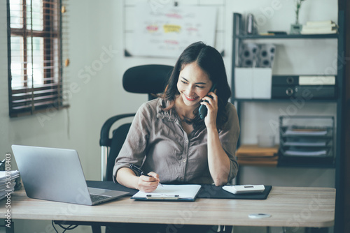 Portrait of a beautiful Asian woman looking at laptop screen while sitting at working desk in the office