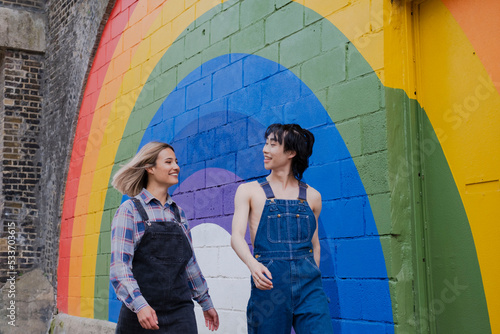 Cheerful young woman and man walking together by rainbow mural on wall photo