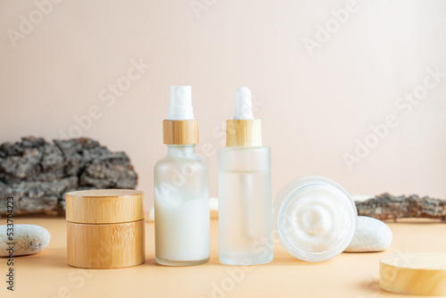 White frosted glass cosmetic bottles and jars with pamboo lids with tree bark, stones on beige background. Skin care routine set for aging skin
