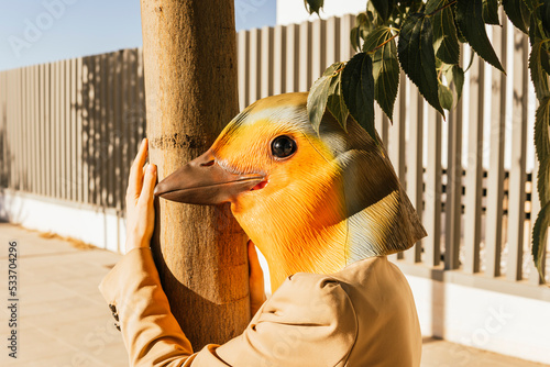 Freelancer wearing bird mask hugging tree at footpath photo