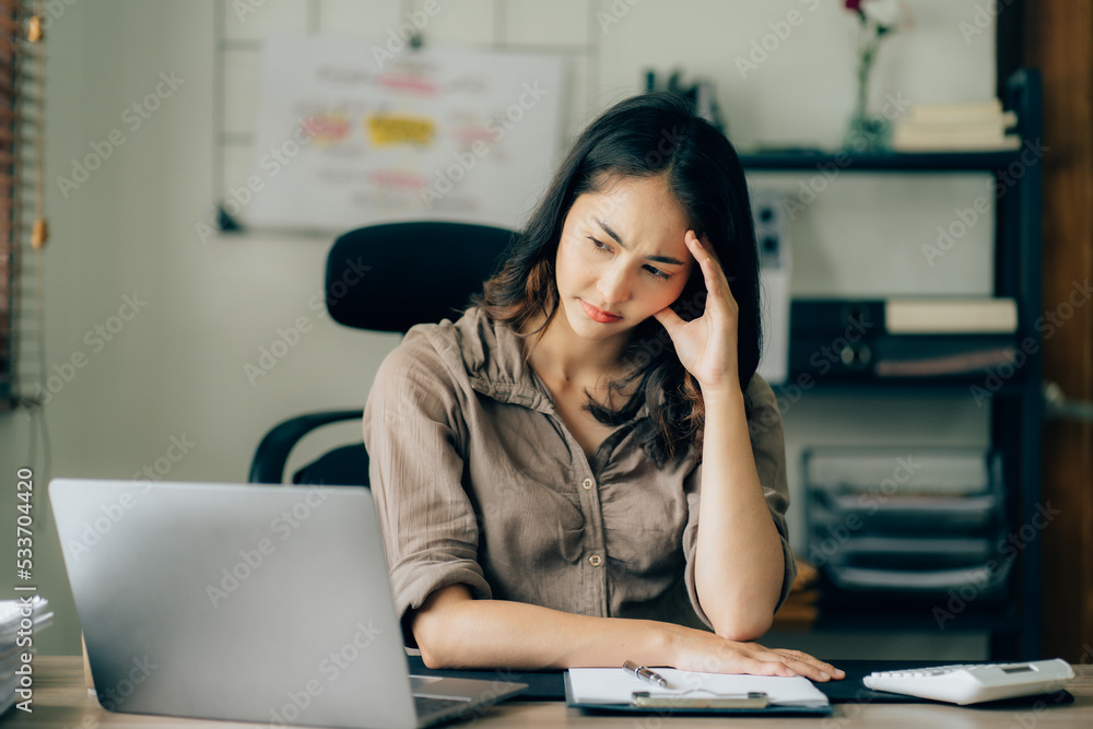 Portrait of a beautiful Asian woman looking at laptop screen while sitting at working desk in the office Portrait of a beautiful Asian woman looking at laptop screen while sitting at working desk in the office