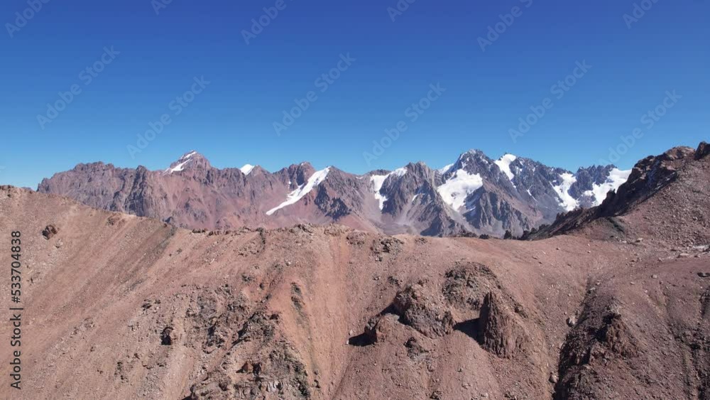 A rocky pass overlooking the snowy mountains. Steep cliffs and big rocks. Blue clear sky. The peaks of the mountains are covered with snow. Top view from a drone. Traces of loose stones. Kazakhstan A rocky pass overlooking the snowy mountains. Steep cliffs and big rocks. Blue clear sky. The peaks of the mountains are covered with snow. Top view from a drone. Traces of loose stones. Kazakhstan