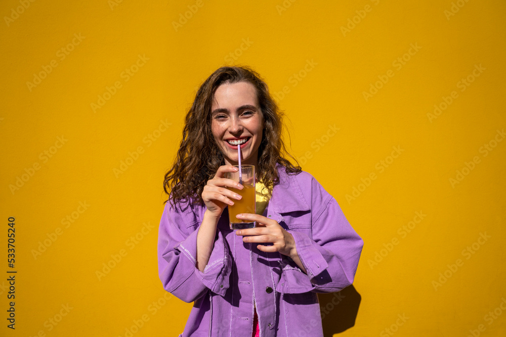 Happy woman drinking orange juice in front of wall Happy woman drinking orange juice in front of wall
