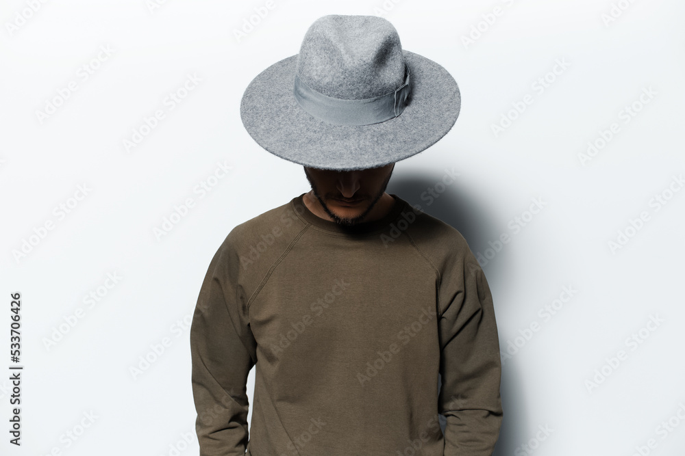 Studio portrait of young man on white background, wearing sweater and grey hat. Looking down.