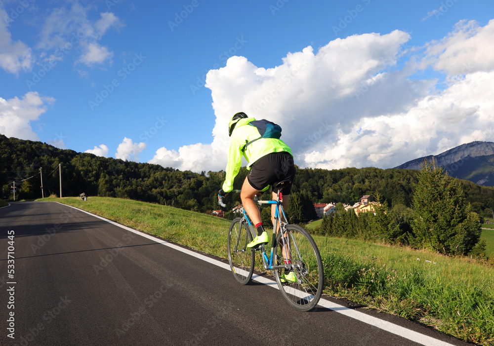 Fototapeta premium cyclist with racing bicycle and phosphorescent waterproof jacket rides fast seen from behind