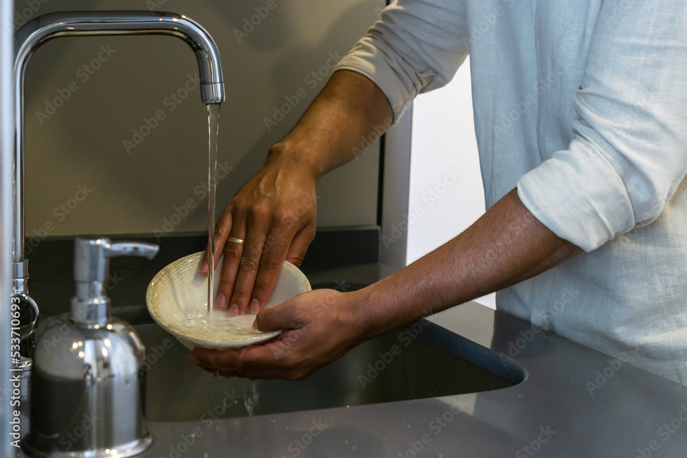 Unrecognizable young man washing dishes in the sink in the kitchen of his home