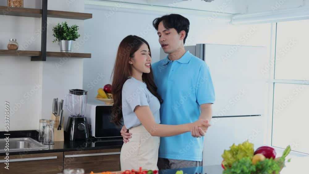 young Asian couple dance together in the kitchen as they cook for breakfast young Asian couple dance together in the kitchen as they cook for breakfast