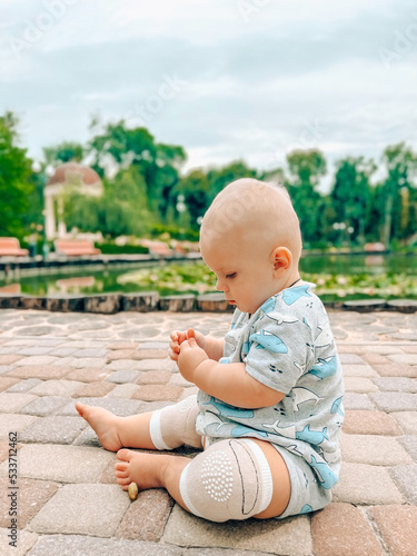Cute baby boy sitting in the park near the lake summer time