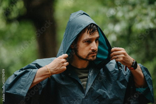 Man wearing a raincoat putting on his hood in the middle of a forest photo