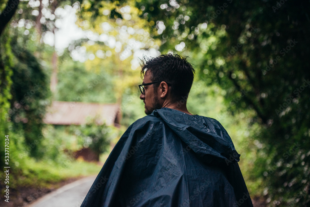 Man wearing a raincoat walking in the middle of a road next to the forest