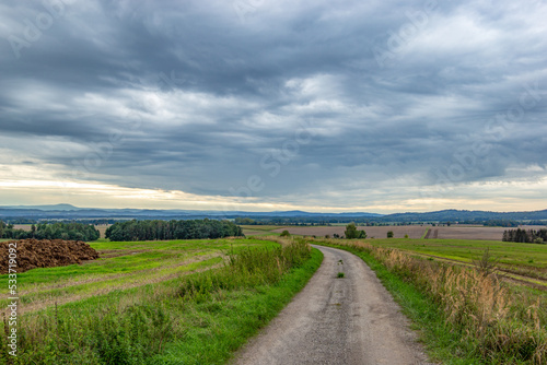 Road through green fields and mountains on a horizon. Early autumn. © Sergey Fedoskin