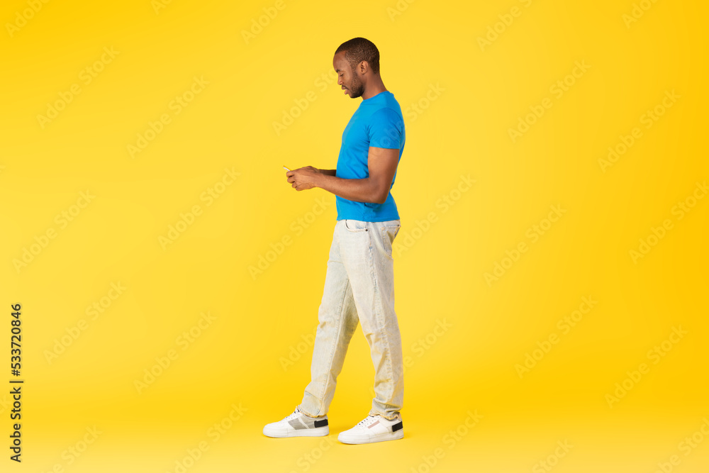 Full Length Of Black Male Using Smartphone Over Yellow Background