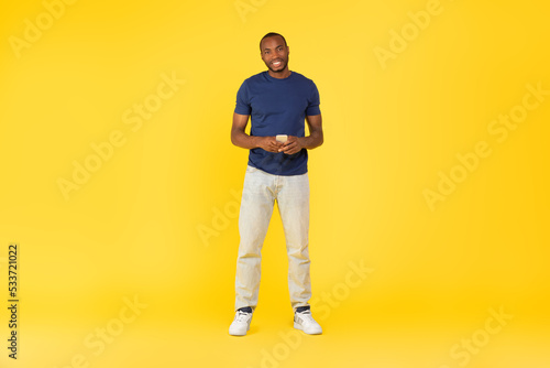 Black Male Using Cellphone Posing Browsing Internet On Yellow Background