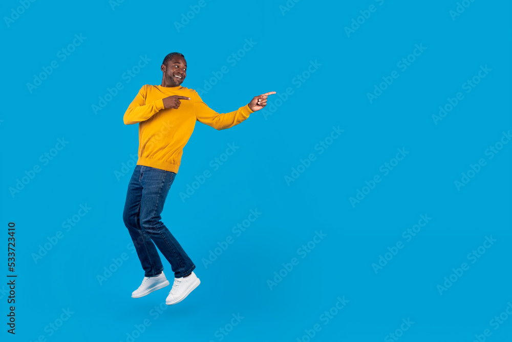 Excited african american man jumping and pointing at copy space
