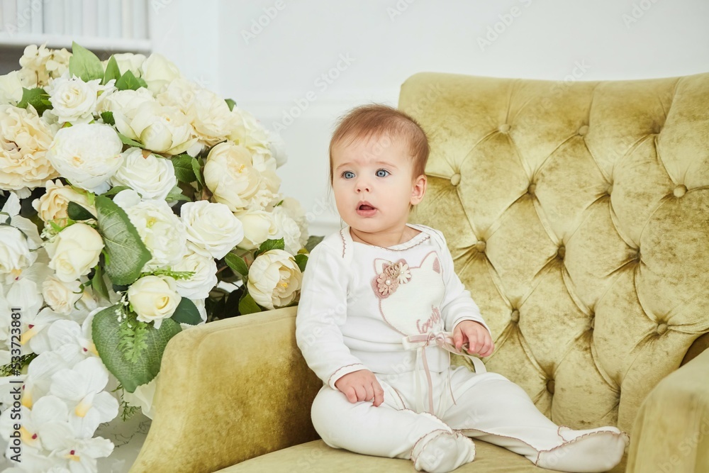 A little baby girl in white clothes is sitting on a chair. The concept of motherhood and childhood. A little baby girl in white clothes is sitting on a chair. The concept of motherhood and childhood.