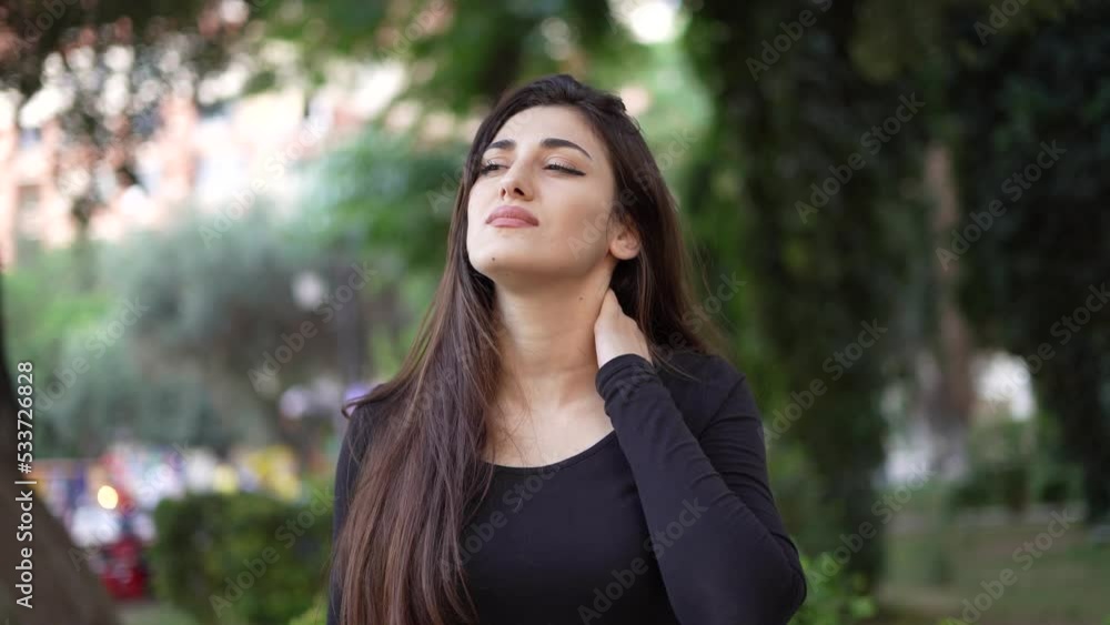 Young woman with neck pain in a park standing outdoors in a park. Young woman with neck pain in a park standing outdoors in a park.