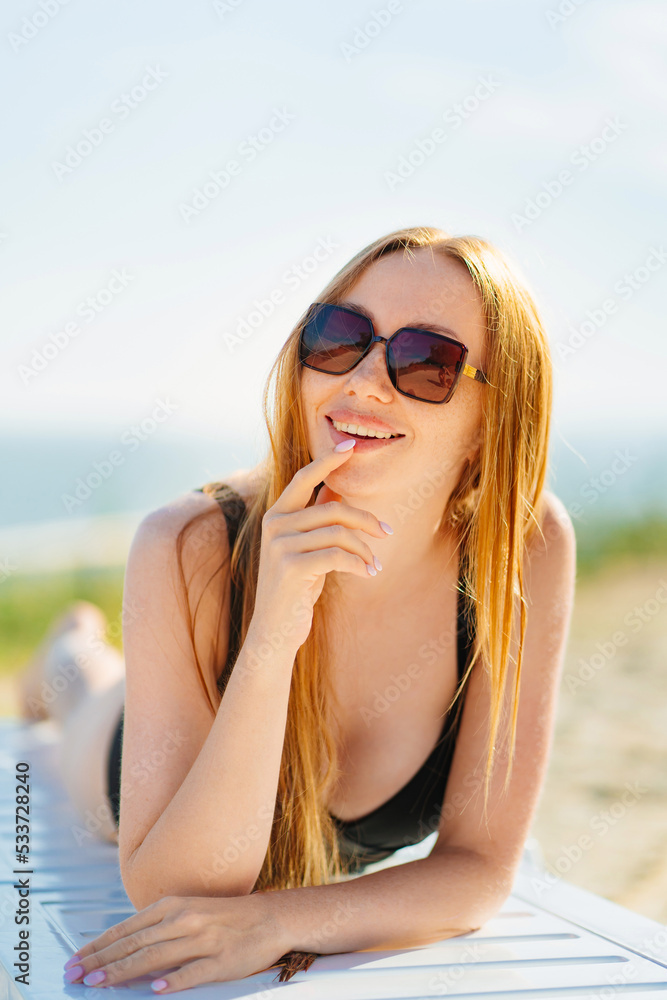 a beautiful woman in sunglasses sunbathing on a chaise longue on a sandy beach a beautiful woman in sunglasses sunbathing on a chaise longue on a sandy beach