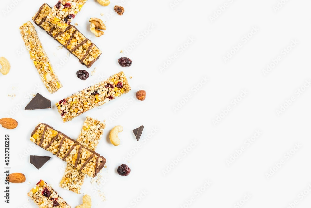 Top view of various homemade granola bars with nuts, seeds, dark chocolate, honey and berries over a white background. Copy space.