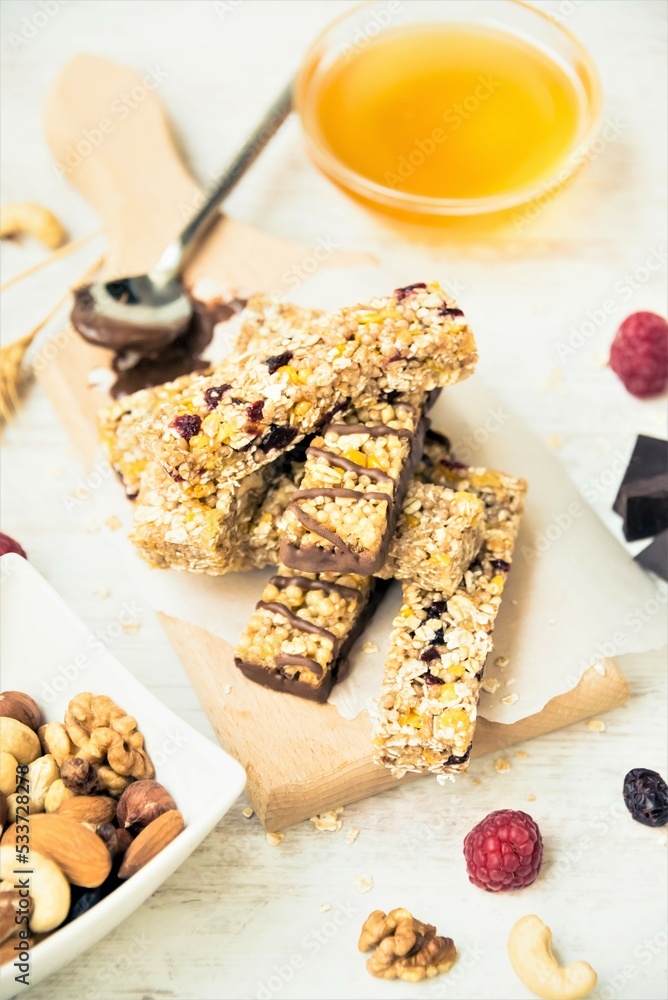 Various homemade granola bars with nuts, seeds, dark chocolate, honey and berries over a wooden board.