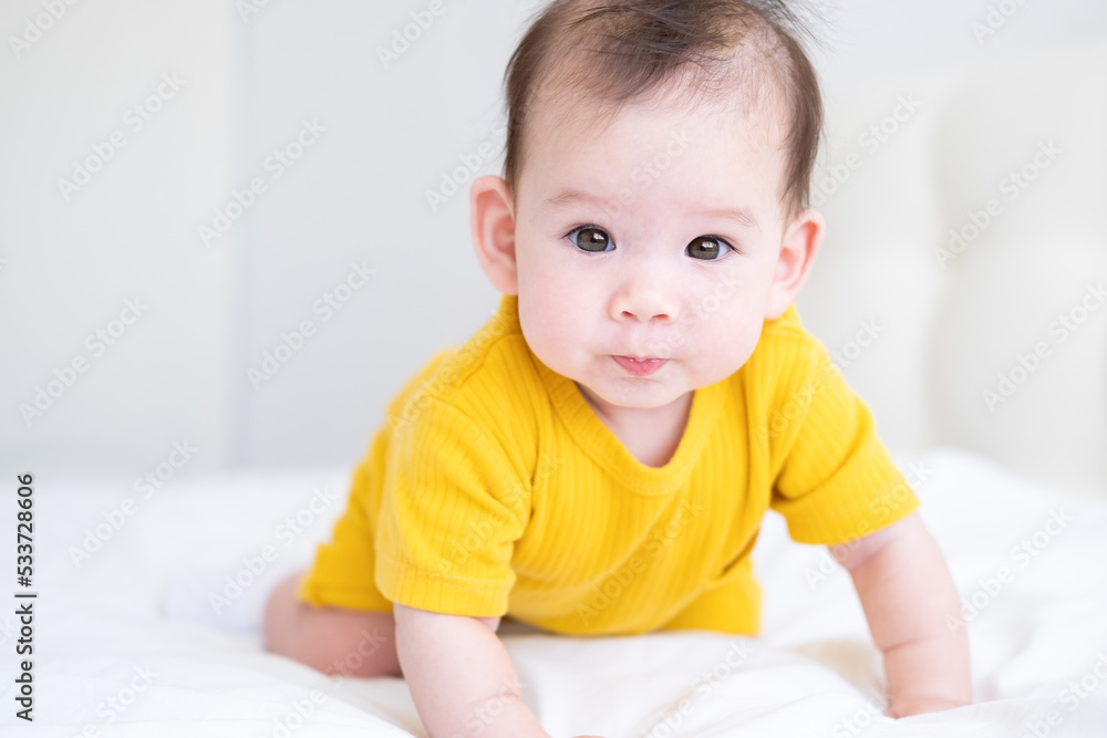 healthy asian baby girl 5 months in yellow bodysuit on bed on white bedding